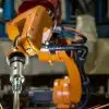 An industrial robot with sparks flying as it welds a metal assembly part for a car on a production line in a modern factory.