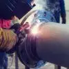 A welder connects a flat welding flange to a steel pipe, creating a secure connection for the piping application.