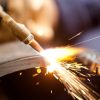 A close-up of a weld head cutting through a large metal pipe with orange sparks coming off of the surface.