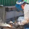 A welder uses a heating rod and filler material to unite a steel pipe at a construction worksite in broad daylight.