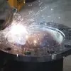 A welder uses a torch to assemble a steel water pipe. The part is thick, and the heat input from the torch is bright.