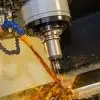 A computer numerical control milling machine cutting material as amber-colored oil coolant splashes around the area.